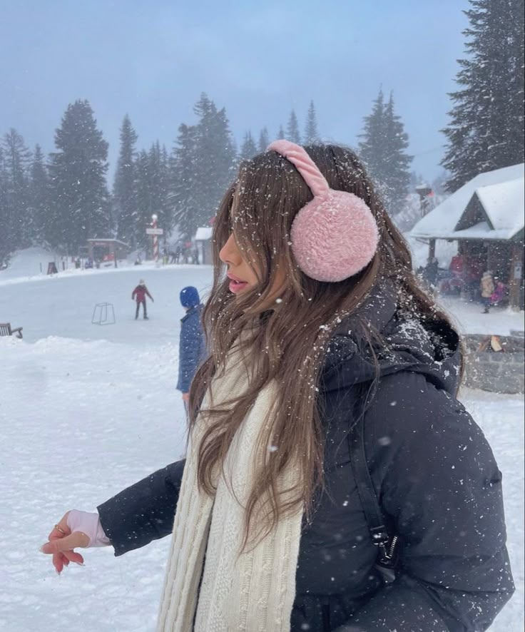 a woman wearing ear muffs standing in the snow with her hand on her hip