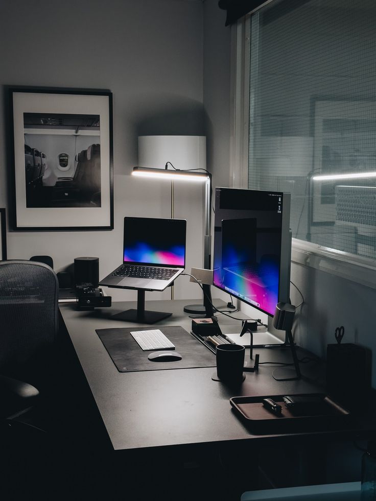 two computer monitors sitting on top of a desk next to a lamp and pictures above them