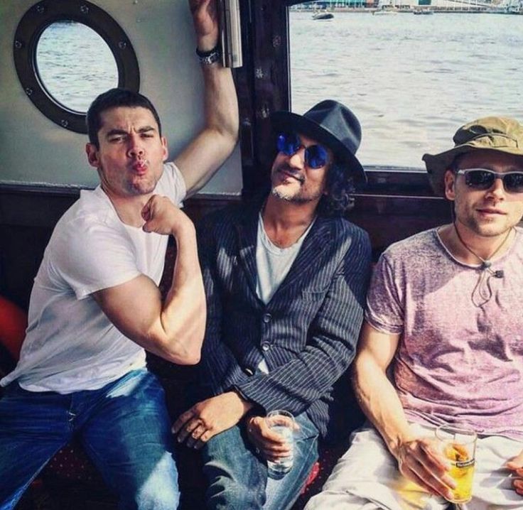 three men sitting next to each other in front of a window on a boat near the water