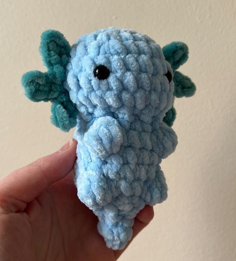 a hand holding a small blue crocheted elephant