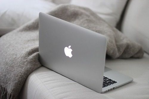 an apple laptop sitting on top of a white couch next to a gray throw blanket