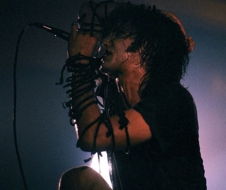 a man with long hair holding a microphone up to his ear while standing on stage