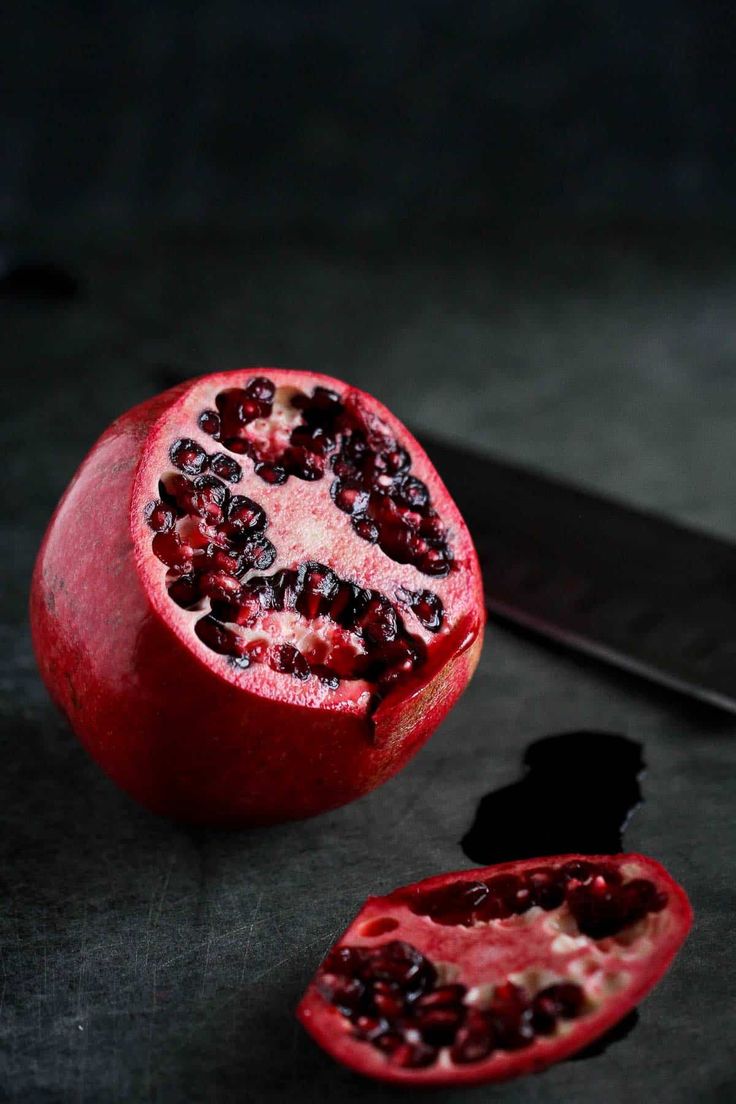 a pomegranate cut in half with a knife on the table next to it