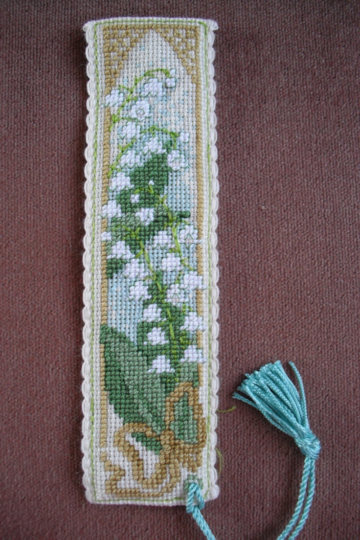 a cross stitch bookmark with white flowers on it and a tasseled cord