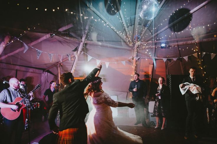 a bride and groom dancing at their wedding reception in a marquee with string lights