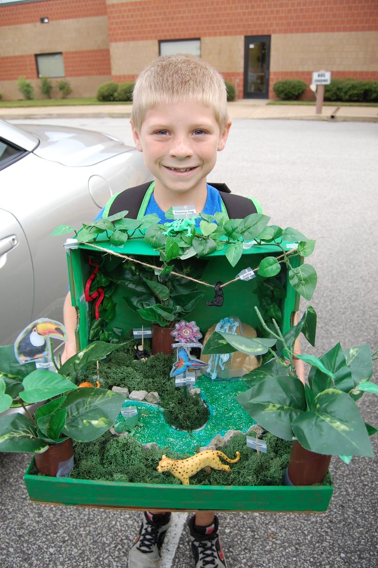 a young boy holding up a fake house made out of plants