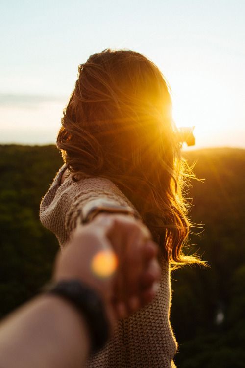 a woman's arm with the sun shining behind her and trees in the background