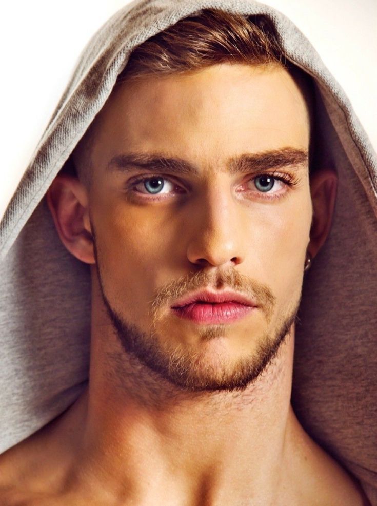 a young man with blue eyes is under a gray towel and looks into the camera