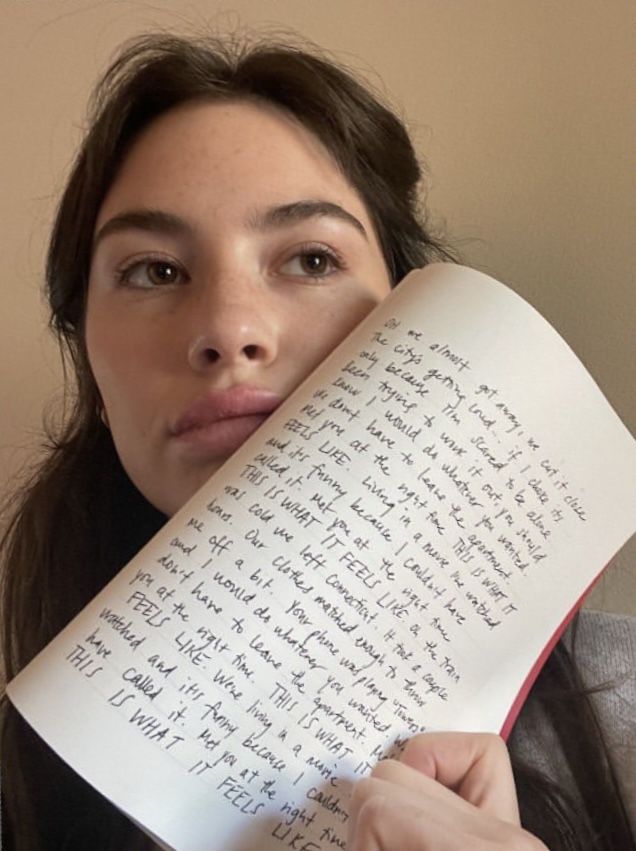 a woman holding an open book over her face with writing on the paper in front of her