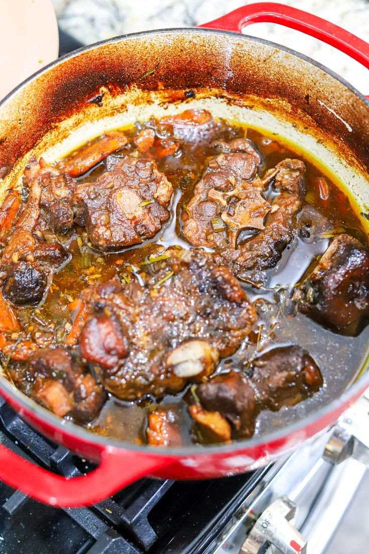 a red pot filled with meat and vegetables on top of an open burner stove