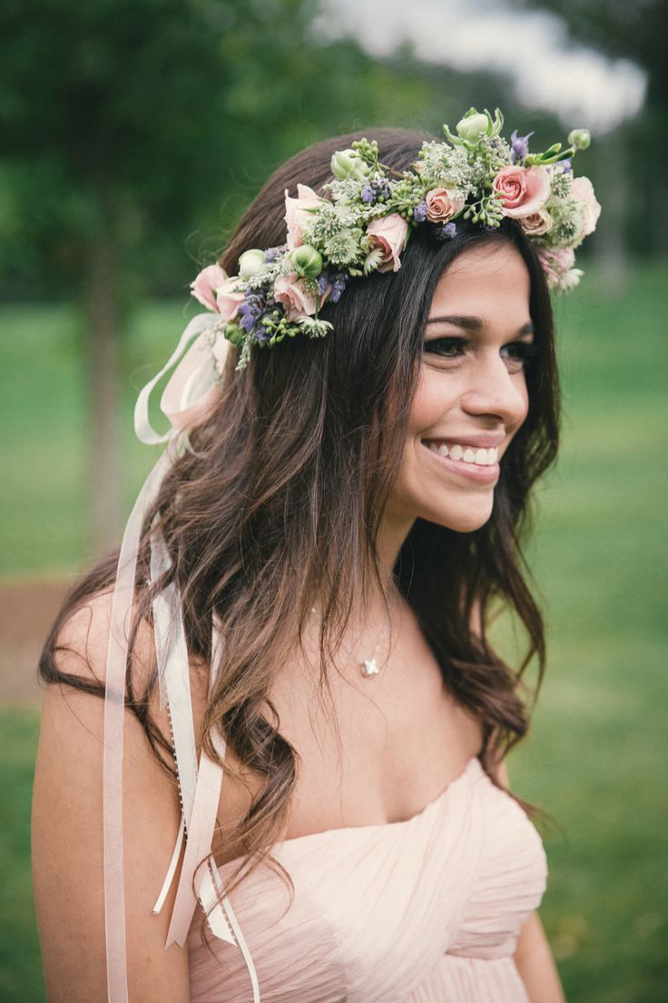 a woman wearing a flower crown smiles at the camera while standing in front of a grassy field