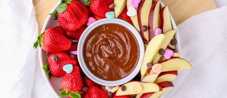 a plate with apples, strawberries, and chocolate sauce on it next to other fruit