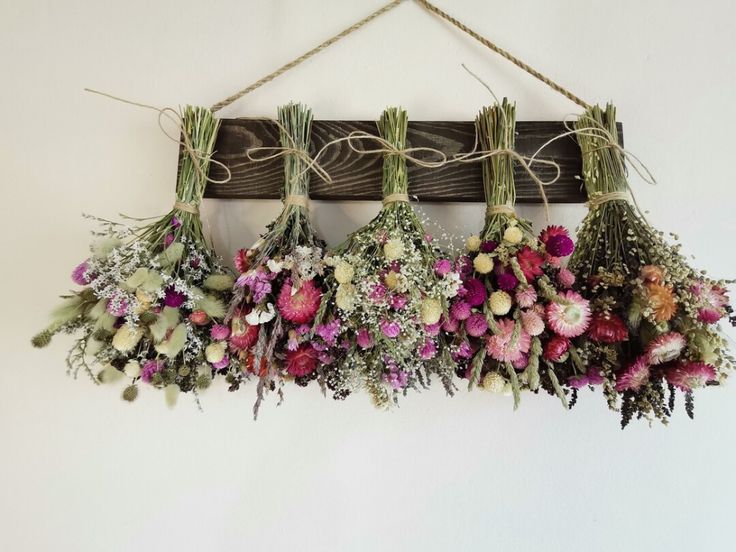 flowers are hanging from a wooden plank on the wall and tied with twine rope