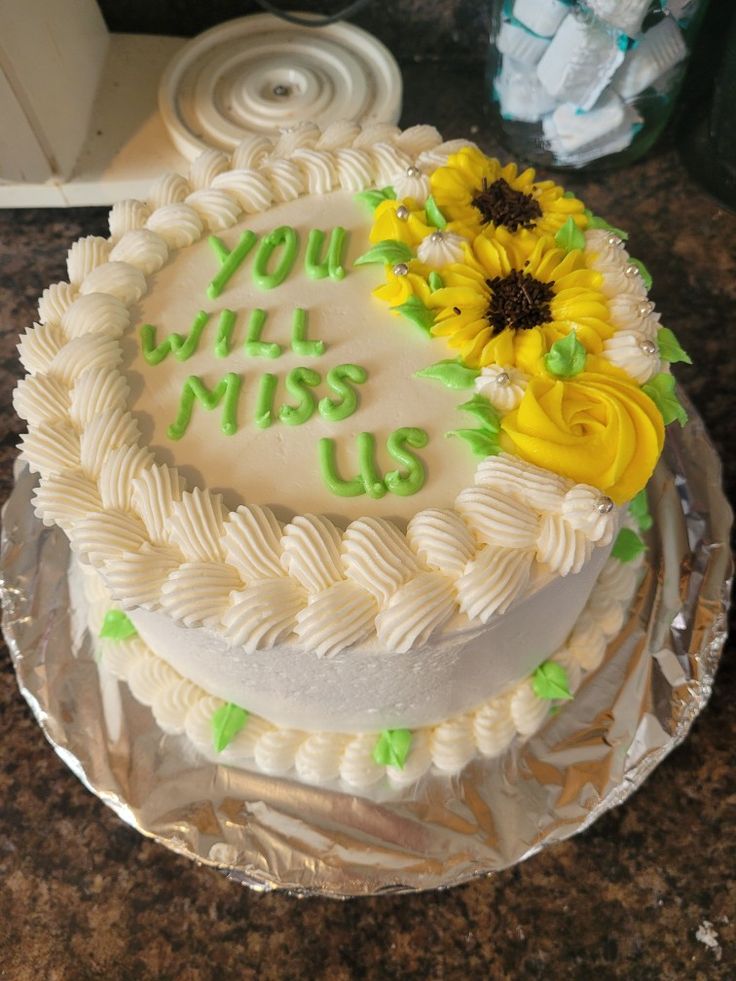 a white cake with yellow flowers on top and the words you will miss us written on it