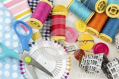 several spools of thread, scissors and measuring tape on a white tablecloth