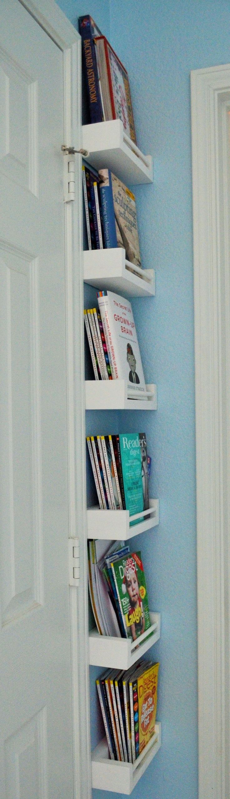 a white book shelf filled with books next to a blue wall in a room that has two doors open