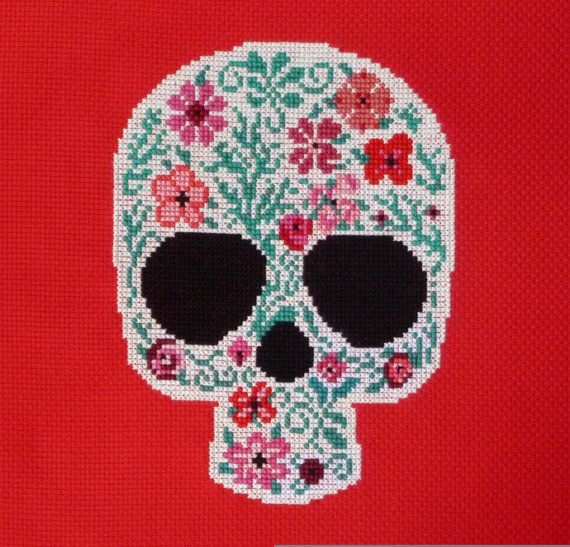 a cross stitch skull with flowers on it's face is shown in white and red