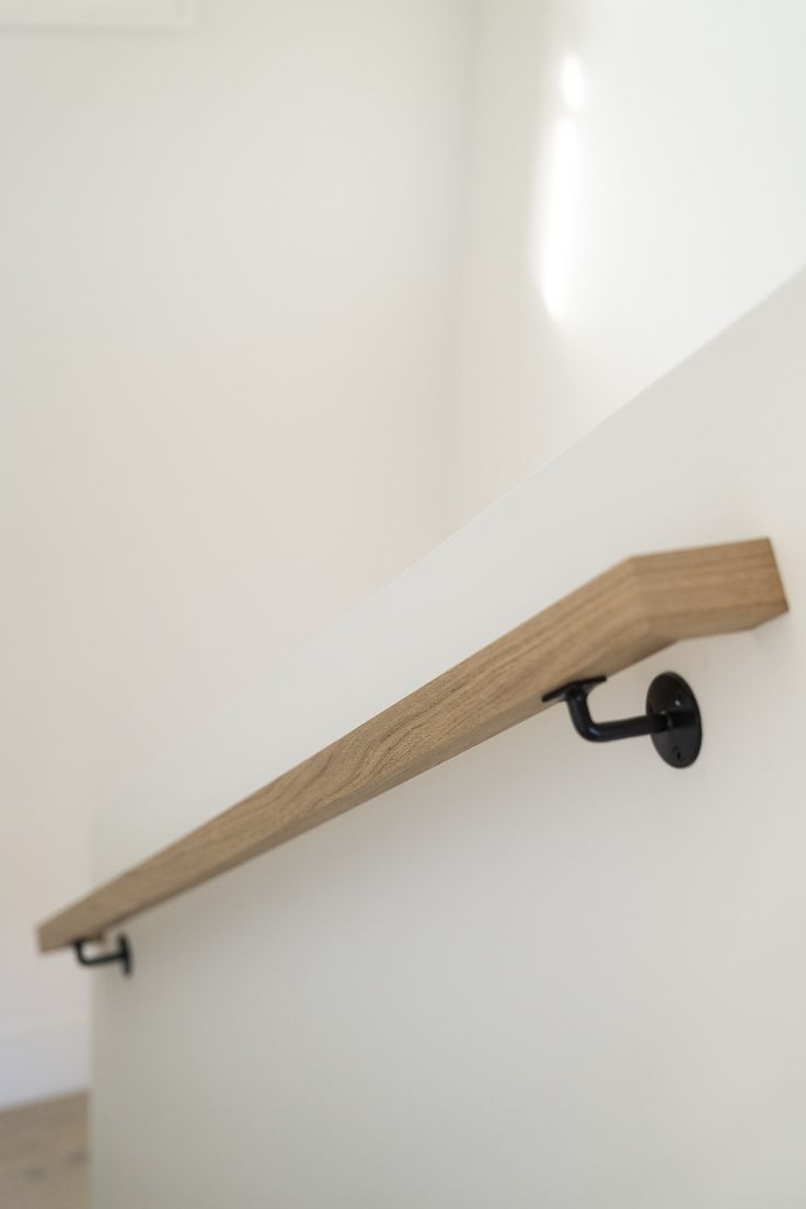 a wooden shelf mounted to the side of a white wall next to a black hook