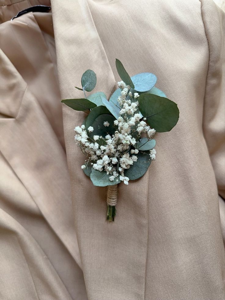 a boutonniere with white flowers and greenery on it's lapel