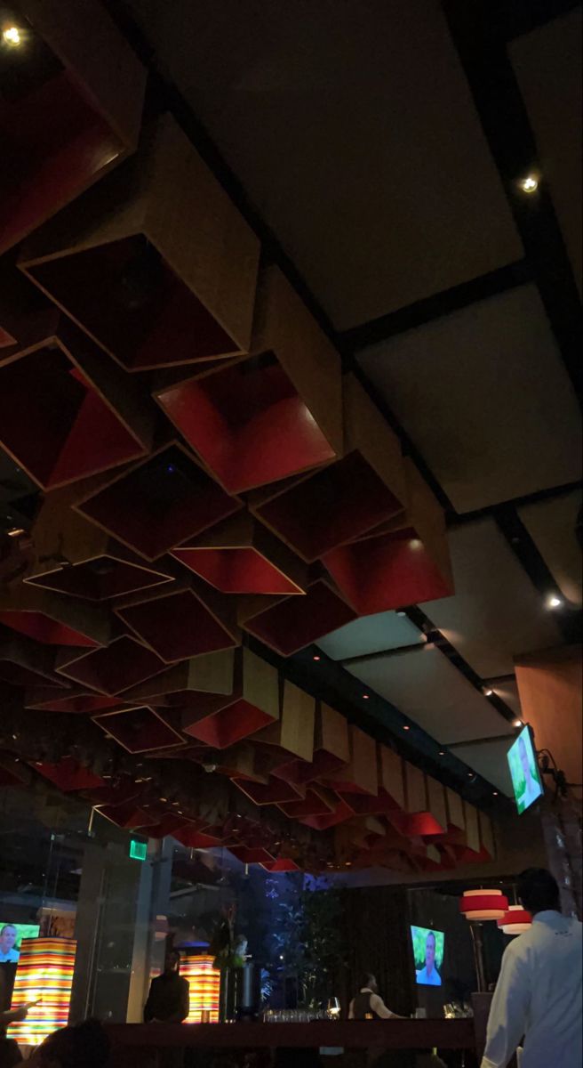 people sitting at tables in a restaurant with red and black ceiling tiles on the walls