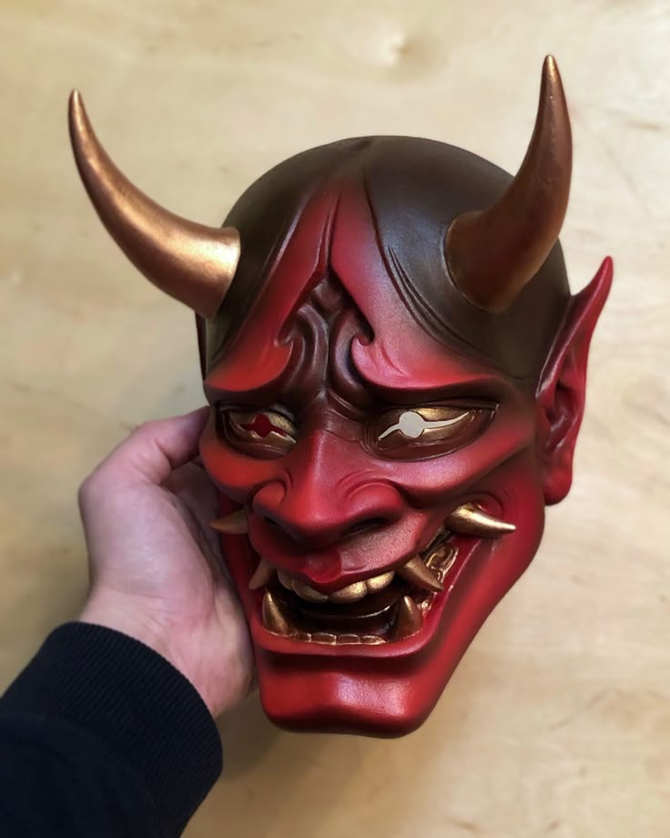 a person holding up a red mask with horns