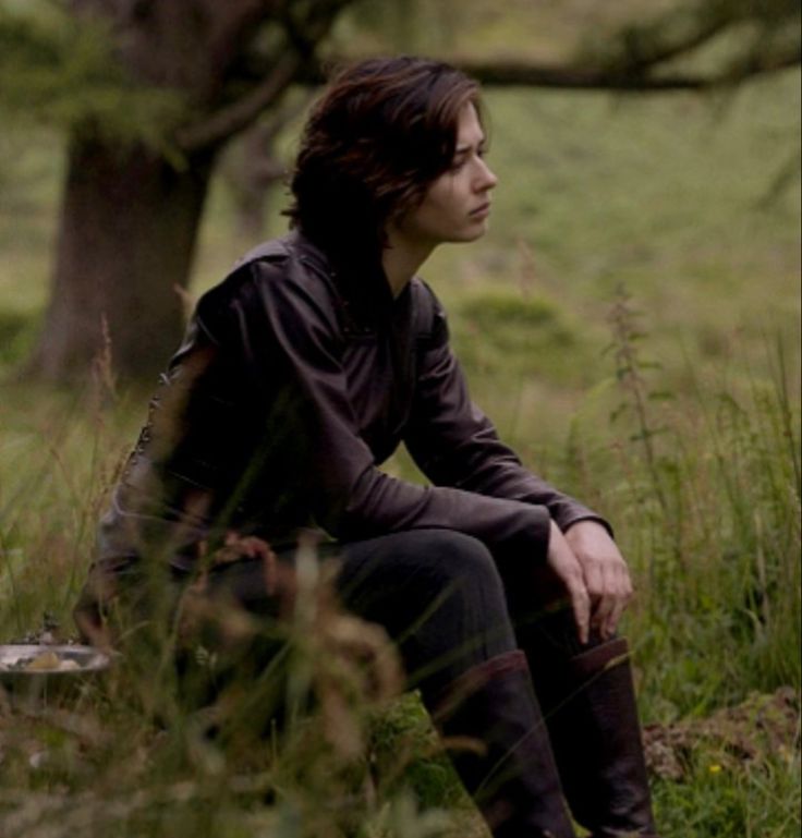 a young man sitting in the grass next to a tree