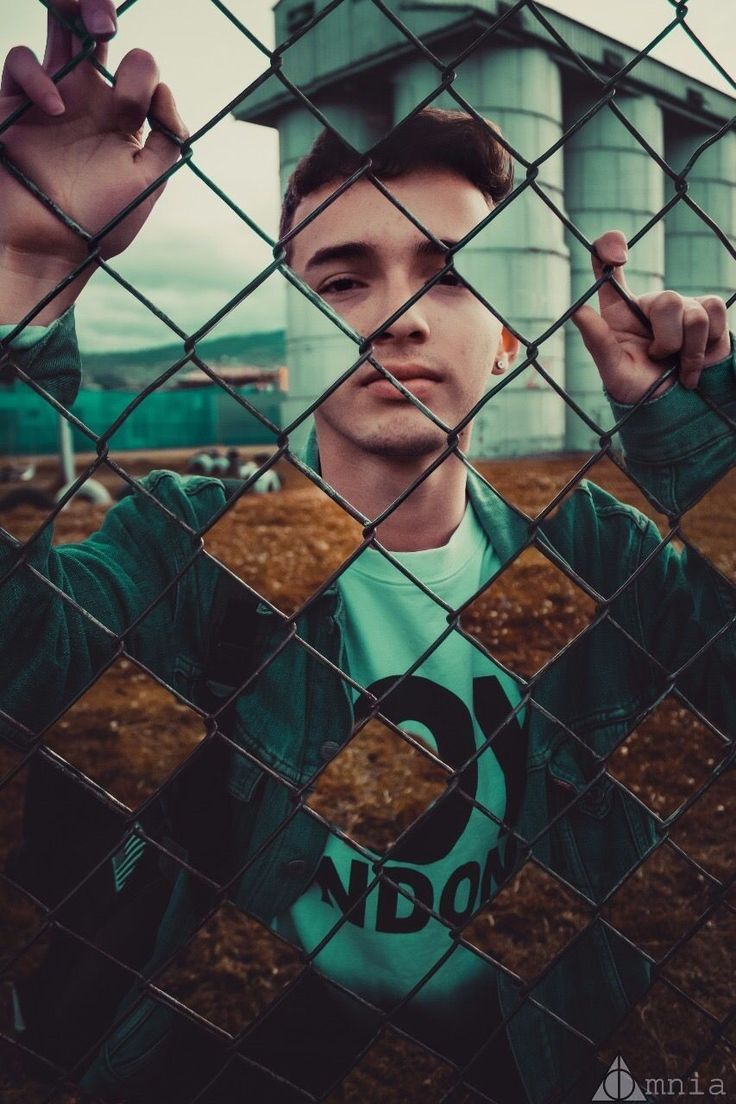 a man standing behind a chain link fence with his hands up in the air and looking at the camera