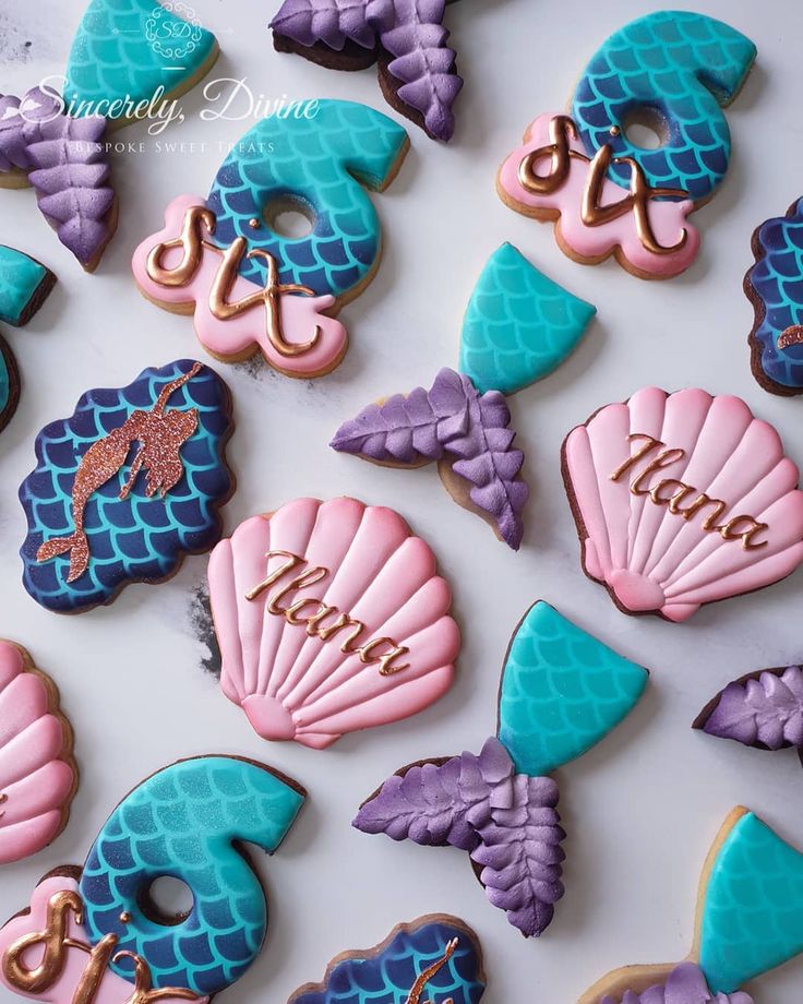 decorated cookies are arranged in the shape of mermaid tails and seashells with names on them