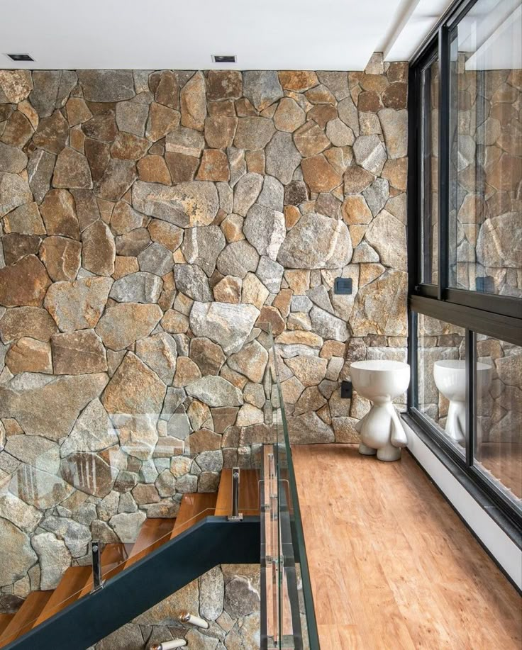 a bathroom with stone wall and wooden flooring next to a glass staircase leading up to the second floor