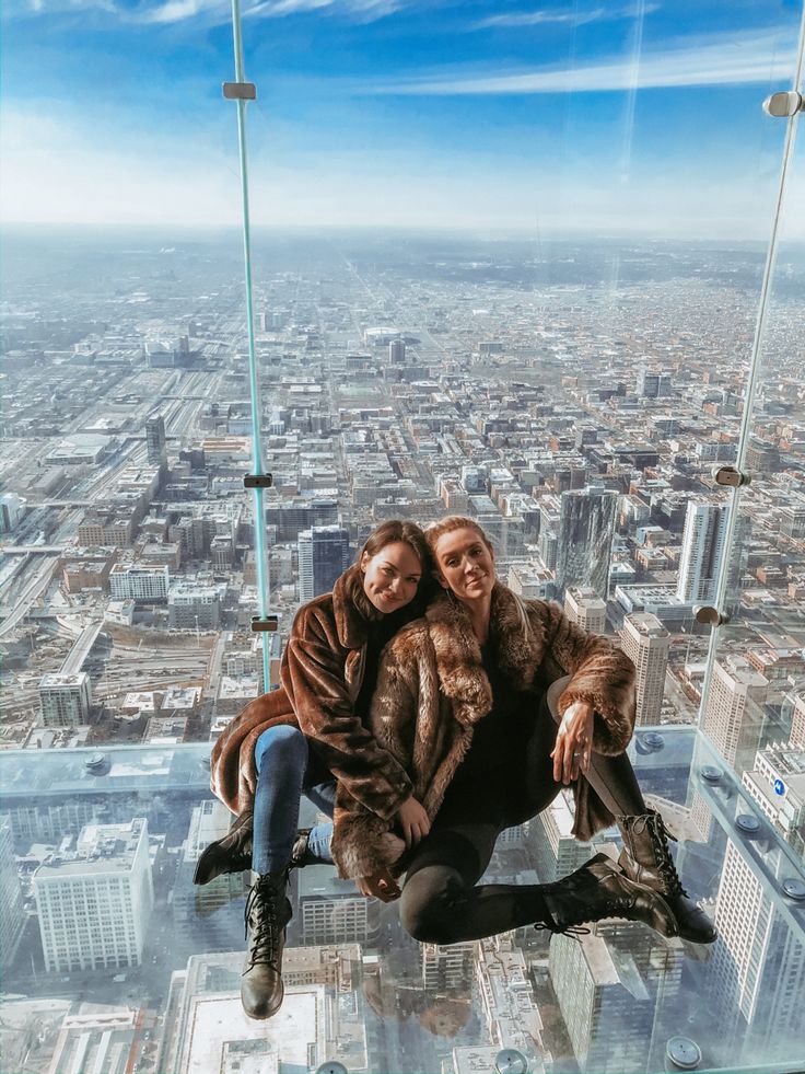 two people sitting on top of a glass floor in the sky tower, with cityscape in the background