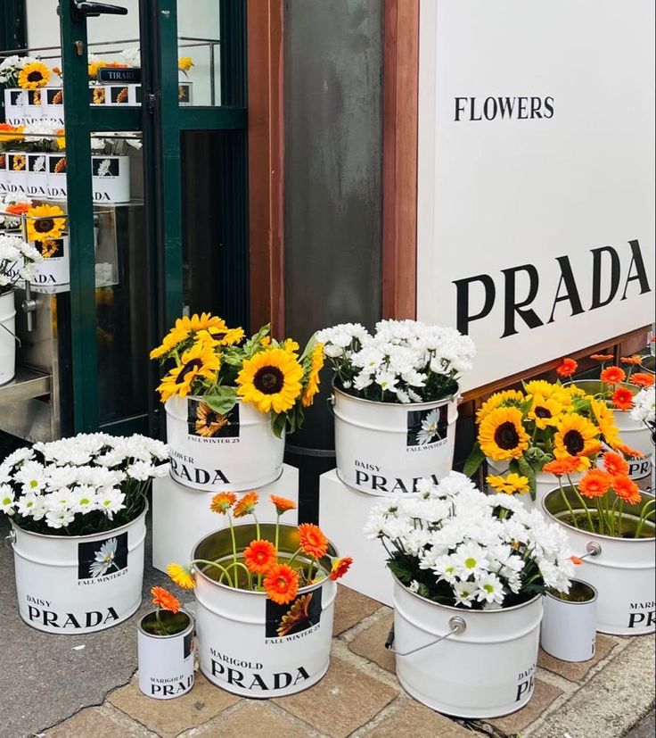 several buckets filled with white and orange flowers on the side of a store front