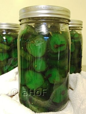 three jars filled with green pickles on top of a white towel