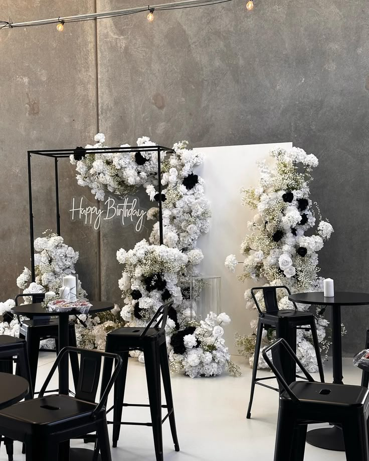 an image of a birthday party setting with flowers on the back wall and black chairs