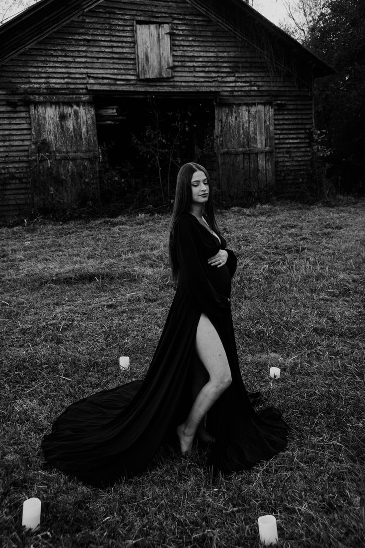 black and white photo of woman in long dress sitting on grass with candles around her