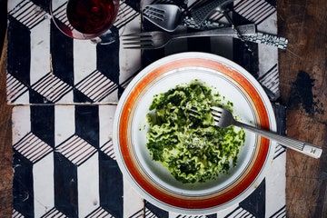 a bowl of food on a table with utensils and wine glasses next to it