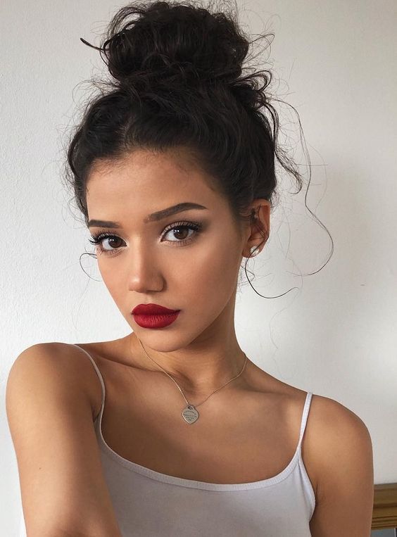 a woman with dark hair and red lipstick wearing a white tank top is looking at the camera