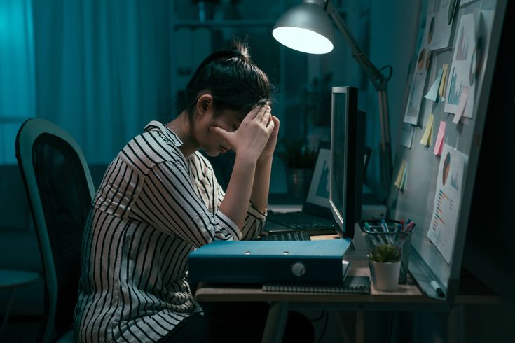 a woman sitting at a desk with her head in her hands while looking at a computer screen