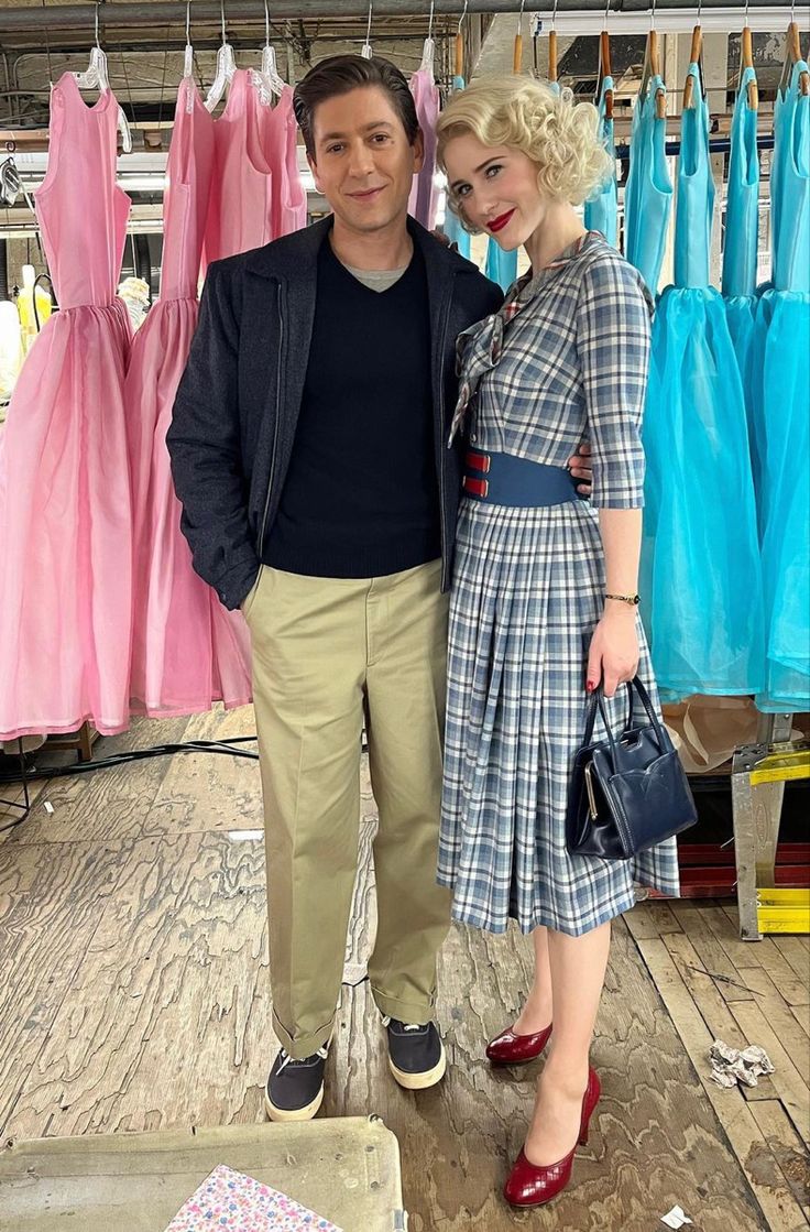 a man and woman standing next to each other in front of dresses on hangers