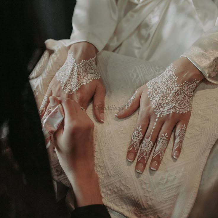 a woman in white dress sitting down with her hands on the back of another person's lap