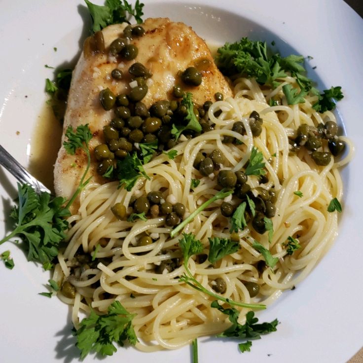 a white plate topped with pasta and meat covered in olives