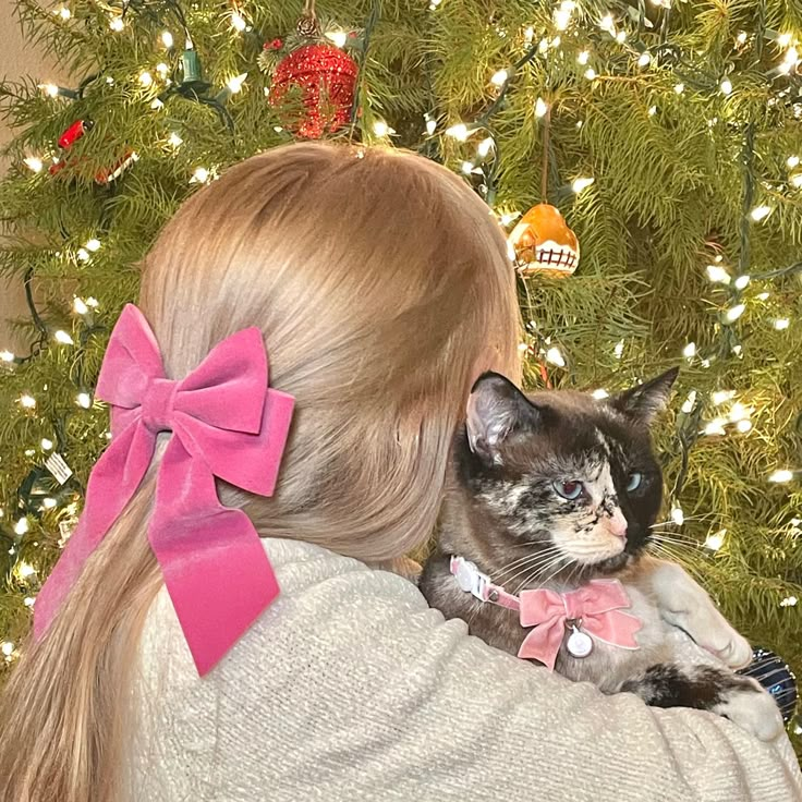 a woman holding a cat in front of a christmas tree