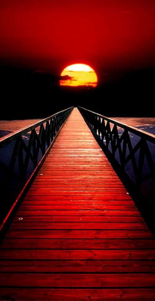 a red wooden bridge with the sun setting in the background