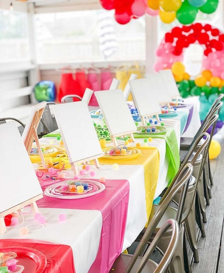 a long table set up for a party with balloons and place cards on it in front of the tables