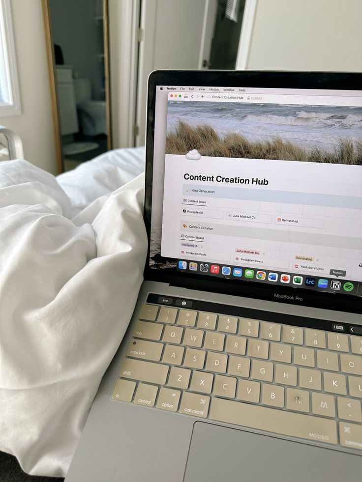 a laptop computer sitting on top of a bed next to a white comforter and pillows