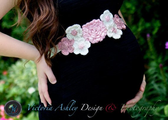 a pregnant woman wearing a black dress with pink and white flowers on the waist, holding her belly