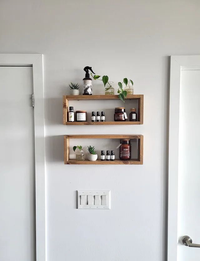 two wooden shelves with plants on them against a white wall in a room that also has a door