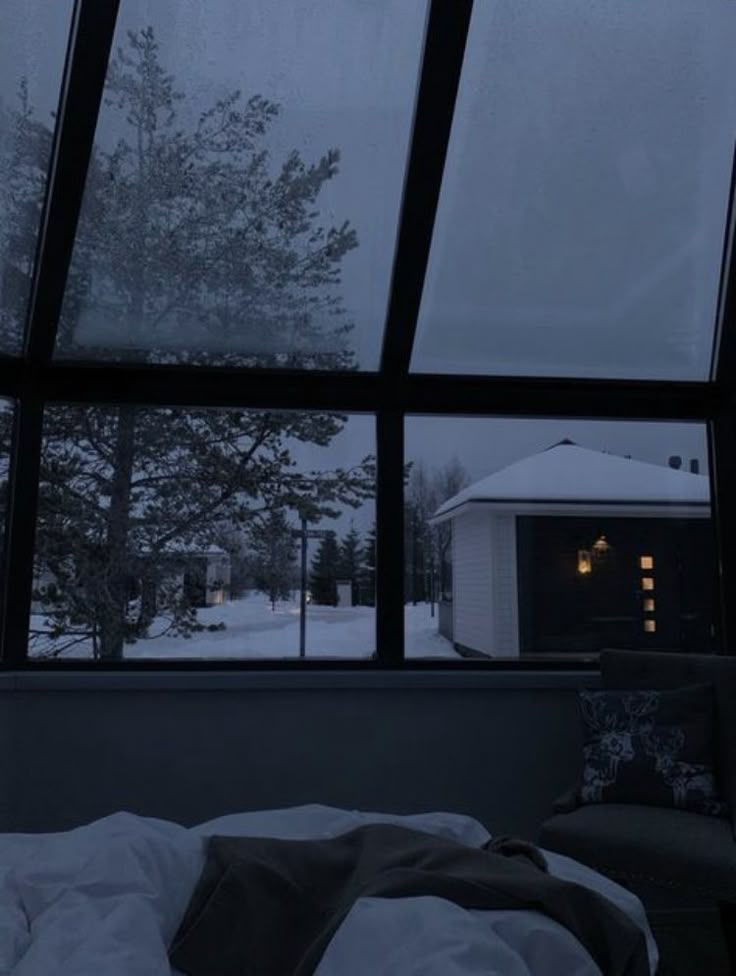 a bed sitting under a large window next to a snow covered forest filled with trees