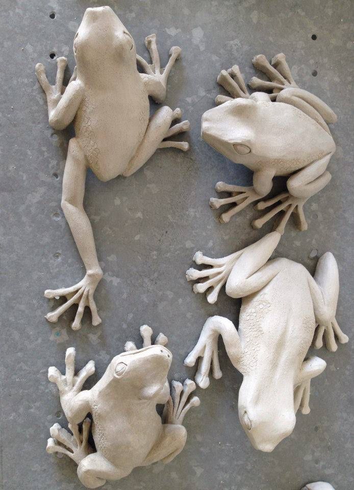 three white frogs sitting on top of each other in front of a gray surface with one frog looking at the camera