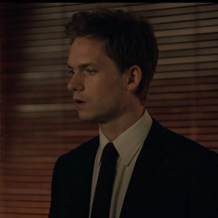 a man in a suit and tie looking off into the distance with blinds behind him