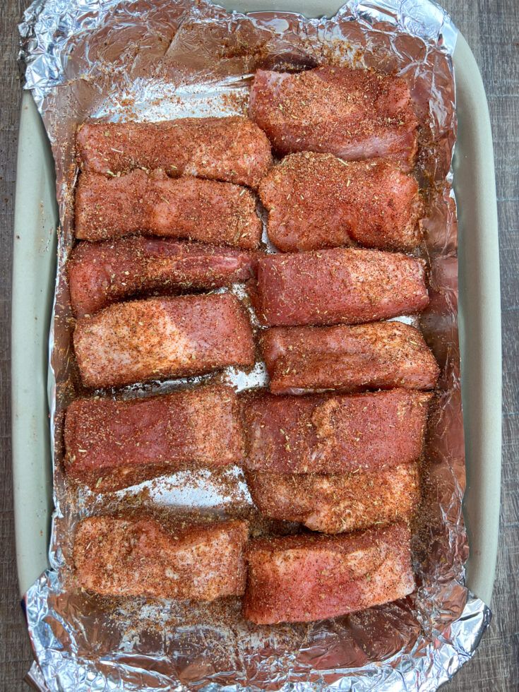 some meat is sitting on tin foil in a baking dish with seasoning sprinkled around it